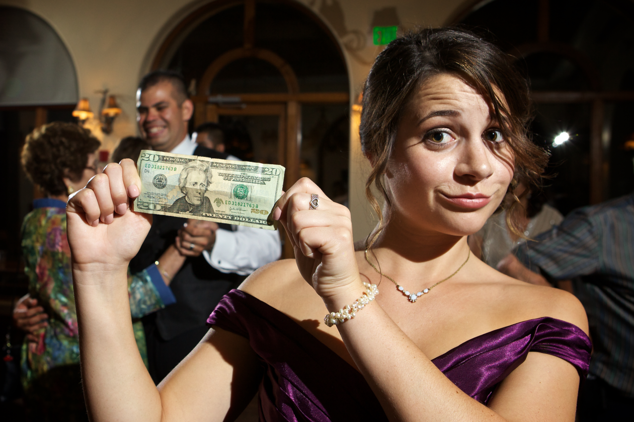 Bridesmaid in purple dress holding up twenty dollar bill for money dance. How to plan a wedding on a budget
