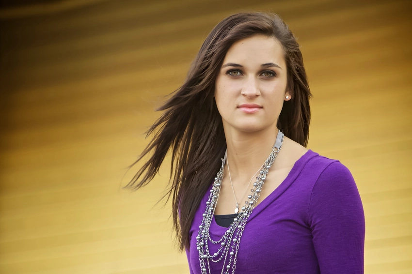 Teen in purple top, hair blowing in breeze, yellow wall in background