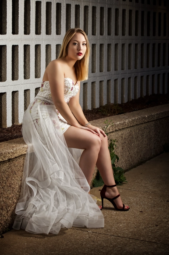 Young woman in flowing white dress sitting on wall