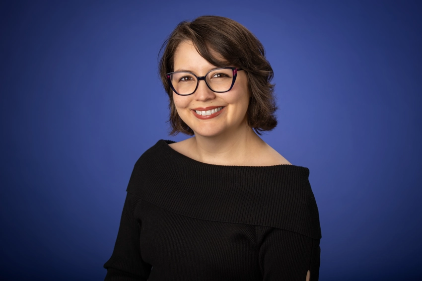 woman with glasses poses in front of a blue background