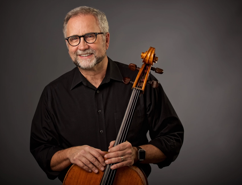 Cello player posing with instrument on grey background