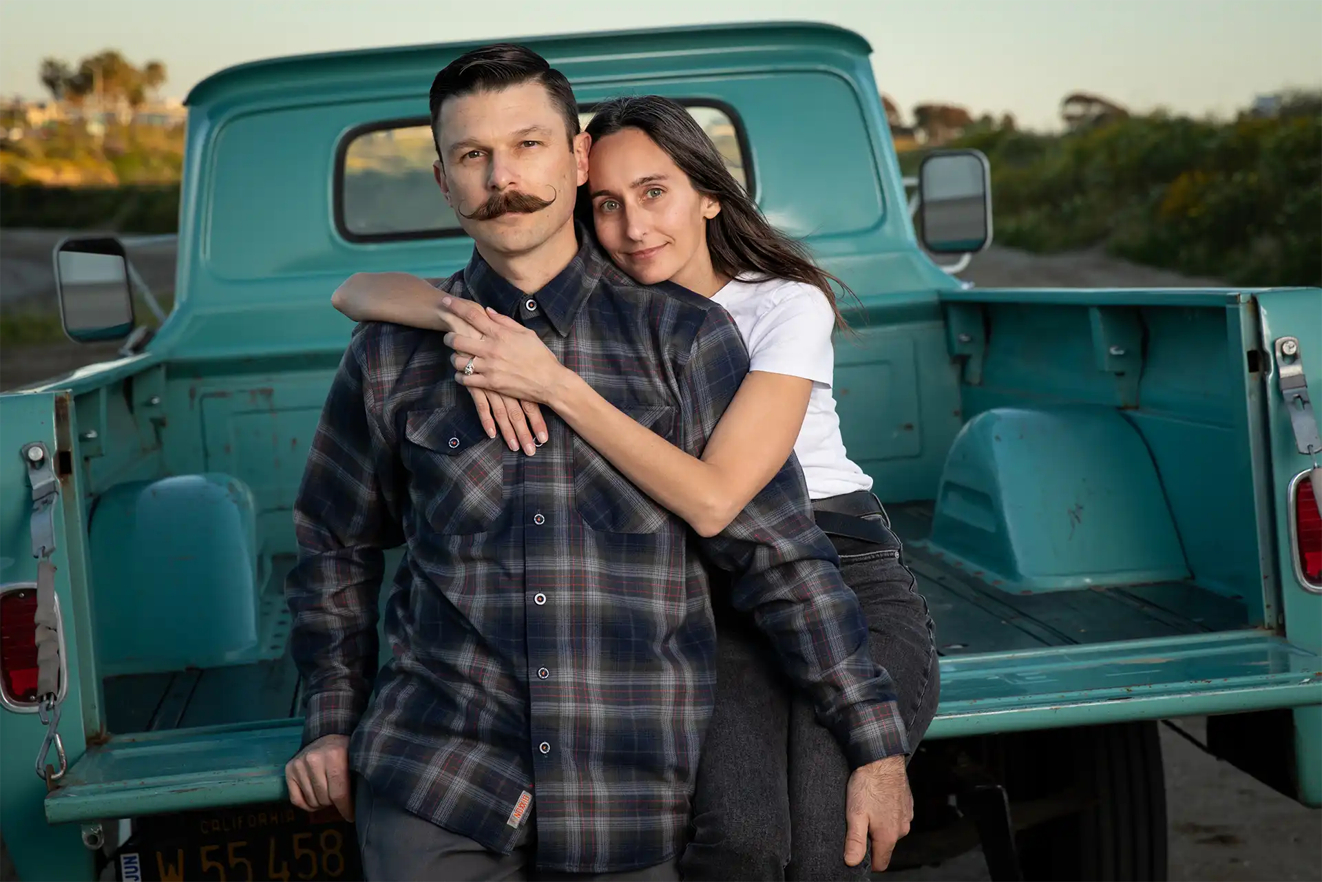 Young couple in an embrace sitting on tailgate of a greenish blue mid 1960s Chevy truck. Tulsa photography