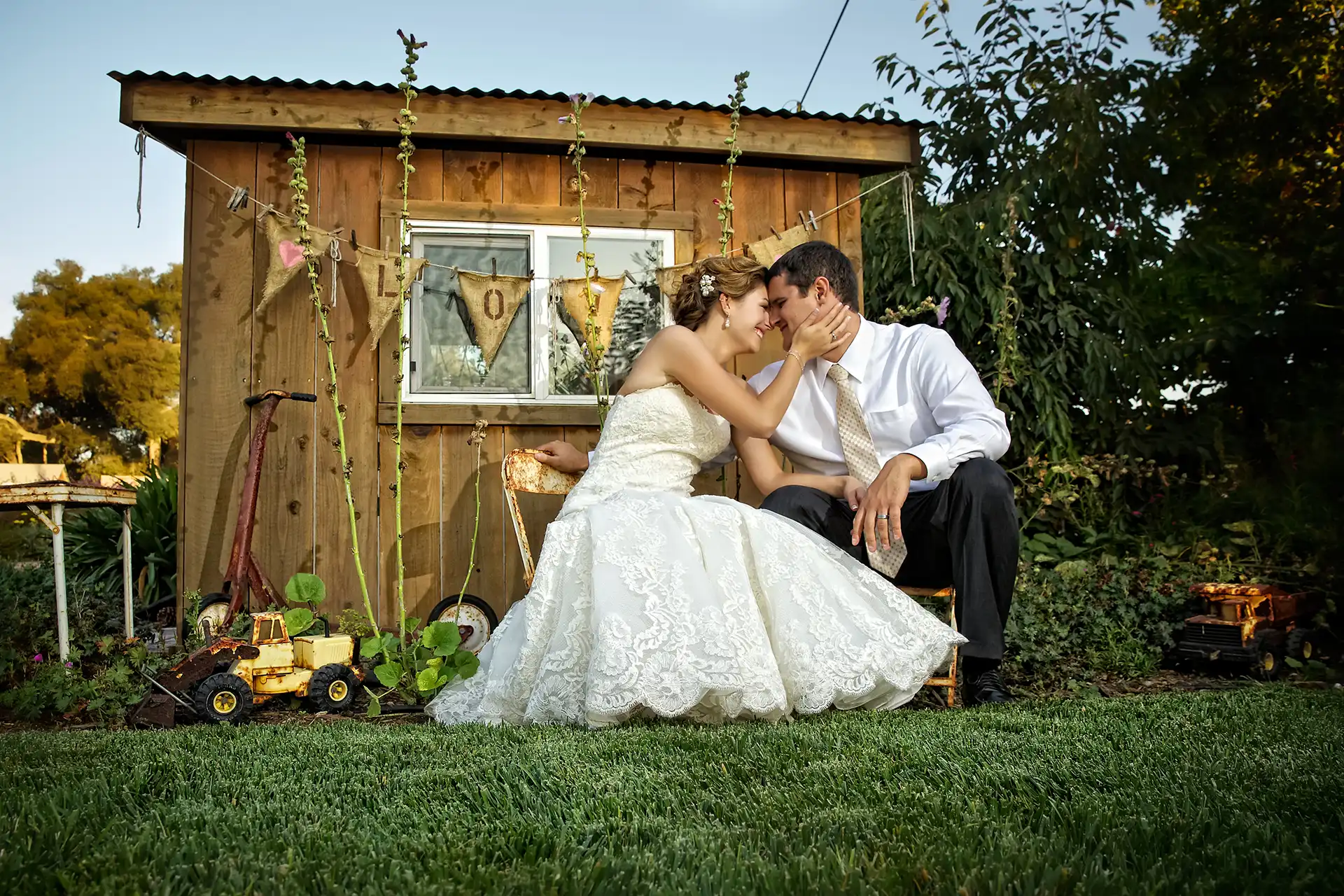 Bride and groom sitting on tiny chairs in front of wooden shack at the gardens at peacock farms. Tulsa photography