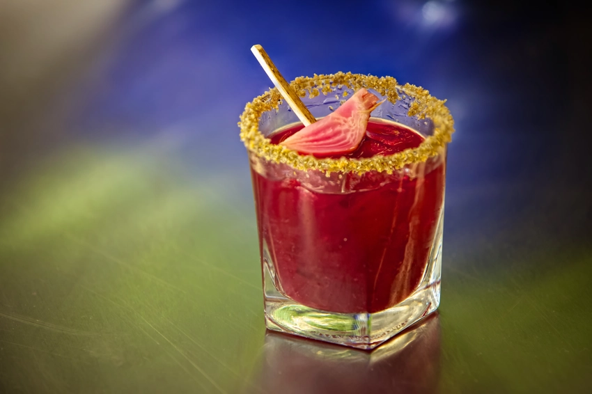 Red cocktail on metal counter reflecting blue and green light