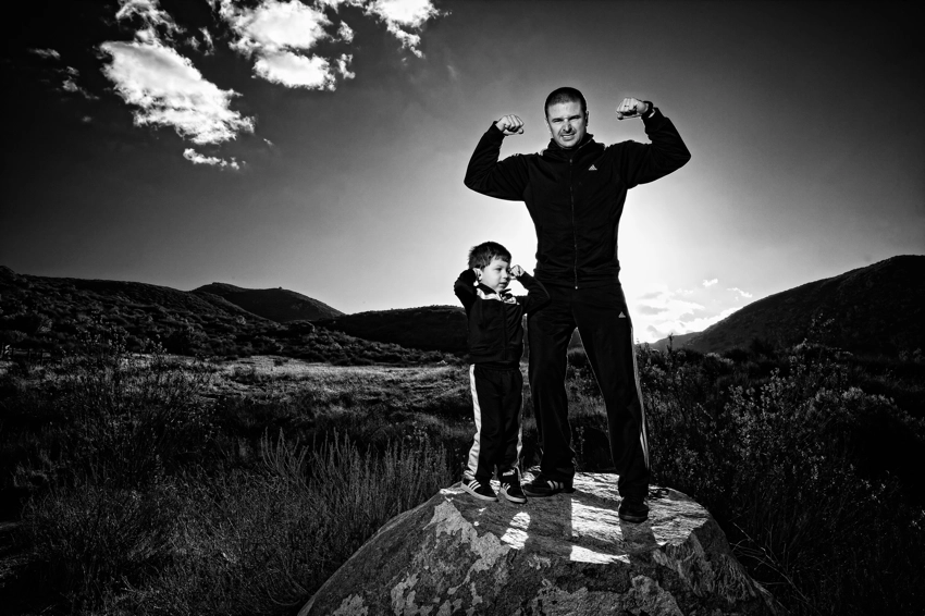 father and son in track suits on rock showing strength, black and white photo